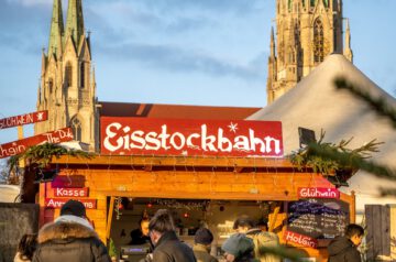 Zu sehen ist die Ausgabehütte auf der Eisstockbahnanlage auf dem Tollwood Winterfestival, welche sich vor allem für Firmenweihnachtsfeiern eignet. Im Hintergrund sieht man die Türme von St. Paul.