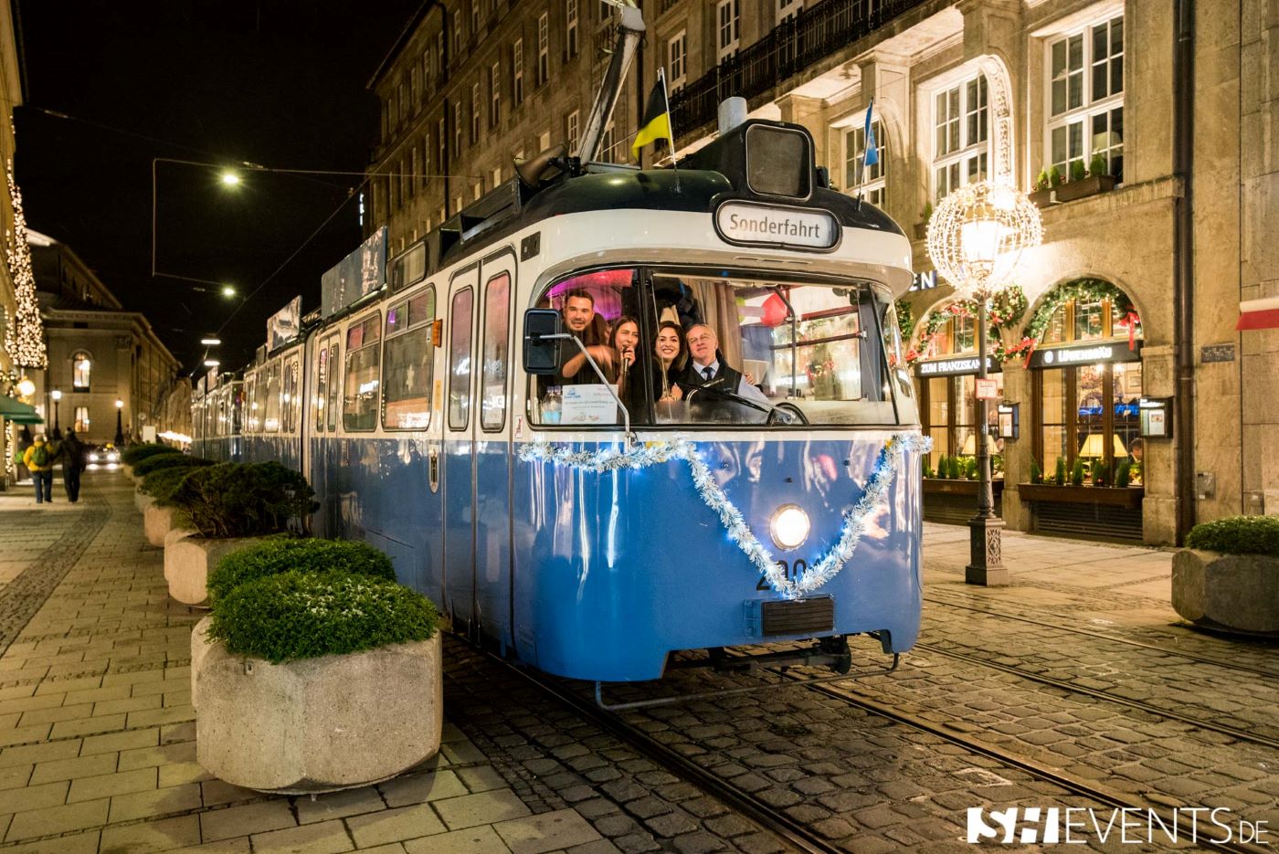 Weihnachtsfeiern 2024 in München: Eine super Idee ist eine Trambahnfahrt. Das Bild zeigt eine historische Tram mit Sonderfahrt-Schild und lachenden Gästen in der Münchner Innenstadt.