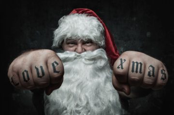 Heavy Metal Weihnachtsfeier: Das Bild zeigt einen kraftvollen Weihnachtsmann mit entschlossenem Gesichtsausdruck. Er streckt seine Hände in typischer Rocker-Manier nach vorne, seine Fäuste sind geballt. Auf seinen Fingern prangt das Tattoo "Love xmas".