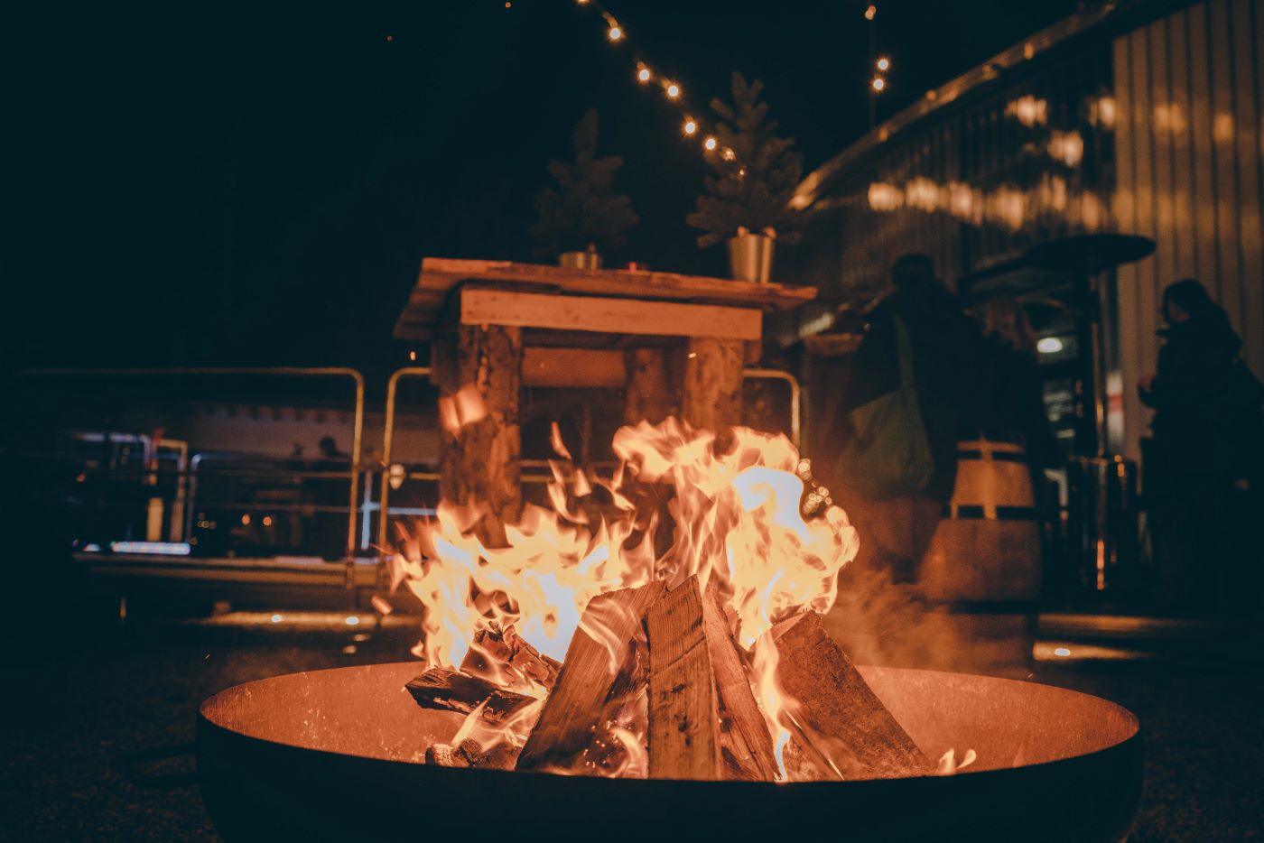 Das Bild zeigt ein Lagerfeuer auf einer Firmenweihnachtsfeier im Außenbereich der Jochen Schweizer Arena. Im Hintergrund seiht man Holzstehtische und weihnachtliche Dekoration.