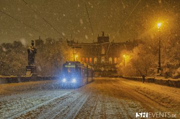 Straßenbahn im Schneefall vor dem Maximilianeum in München, festlich beleuchtet in der Abenddämmerung.