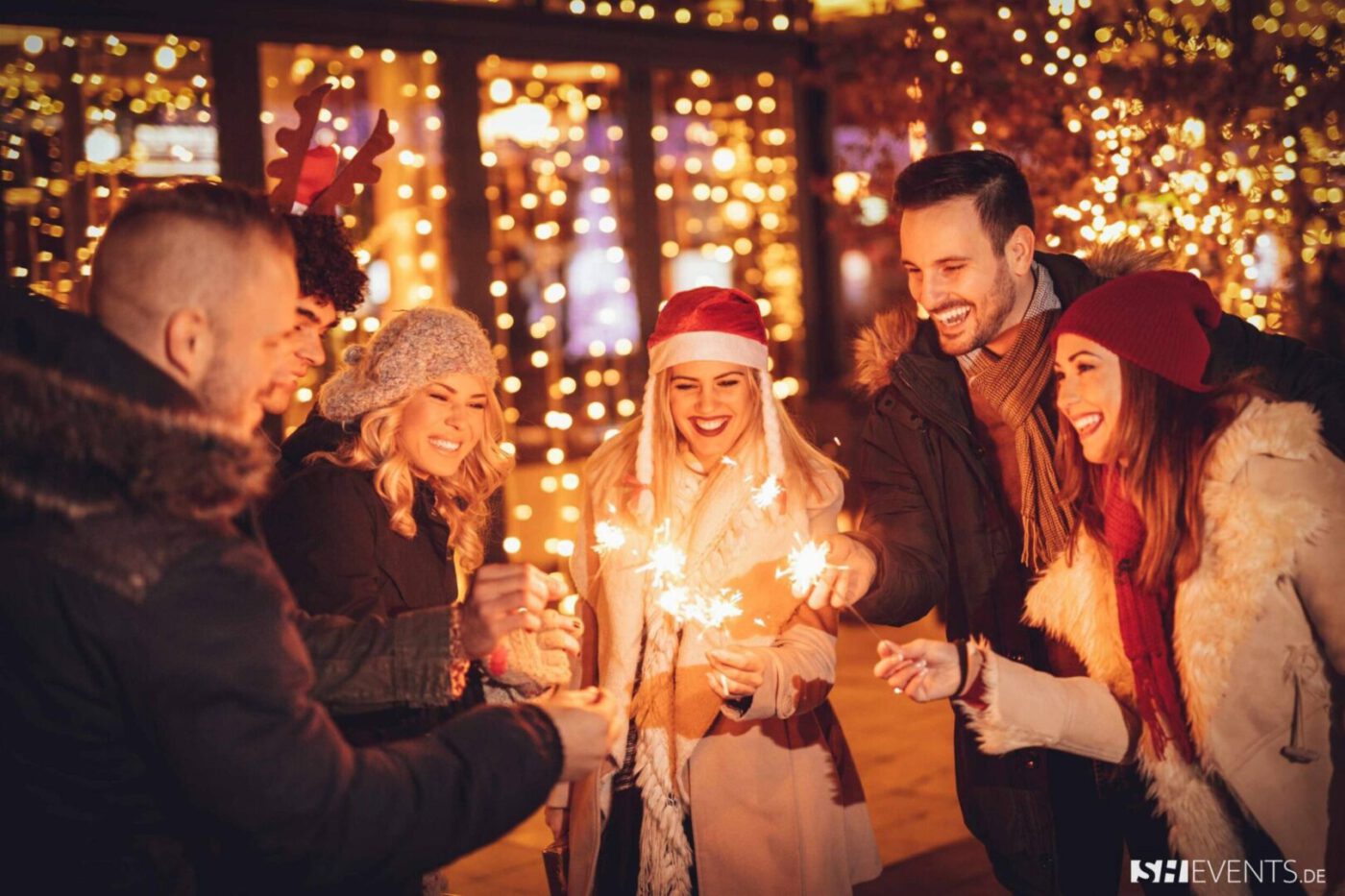 Fröhliche Gruppe mit Wunderkerzen auf einem festlich beleuchteten Weihnachtsmarkt – stimmungsvolle Idee für ihre Weihnachtsfeier 2025.